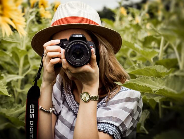 a young lady wearing a hat taking a photograph
